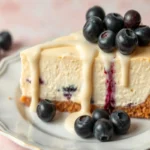 A slice of white chocolate blueberry cheesecake topped with fresh blueberries and sauce.